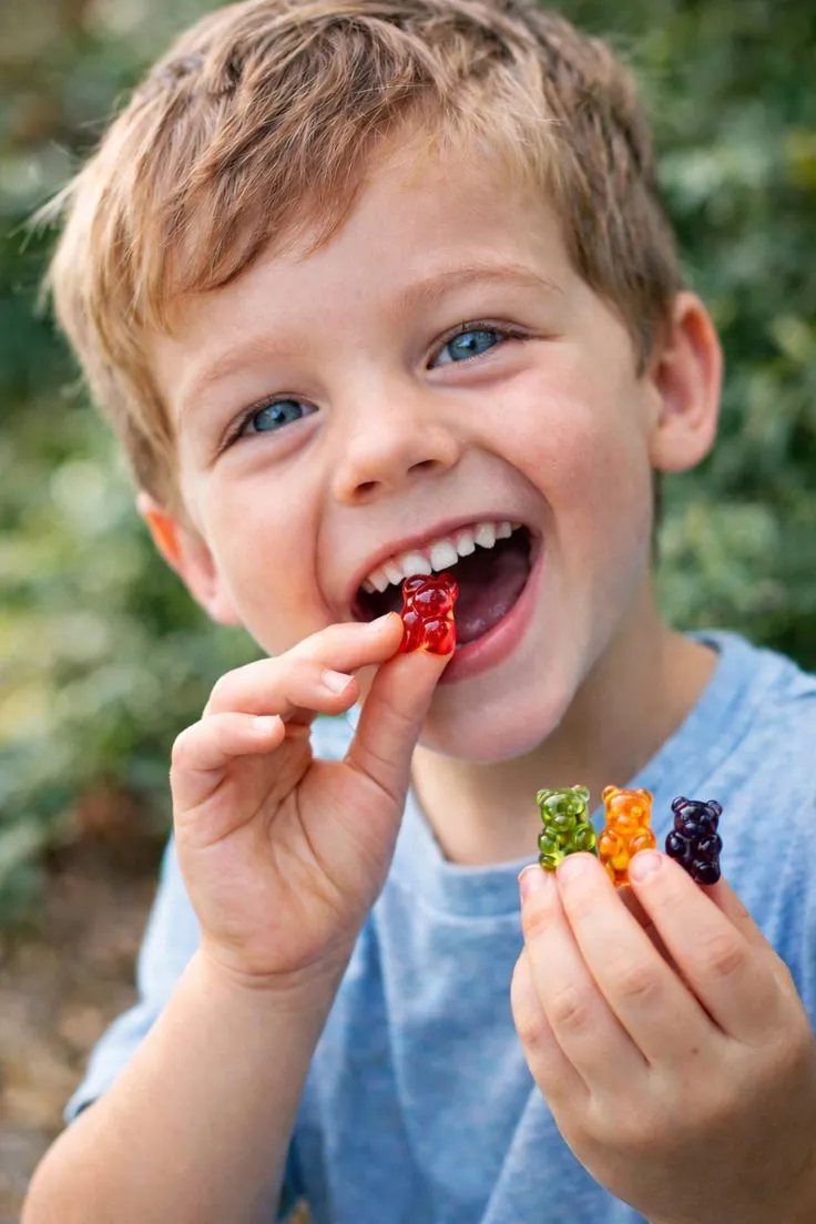 A young boy grins while eating a red gummy bear