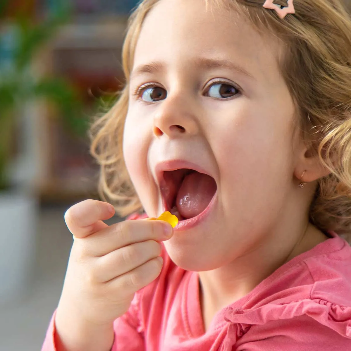 A little girl opens wide for an orange gummy