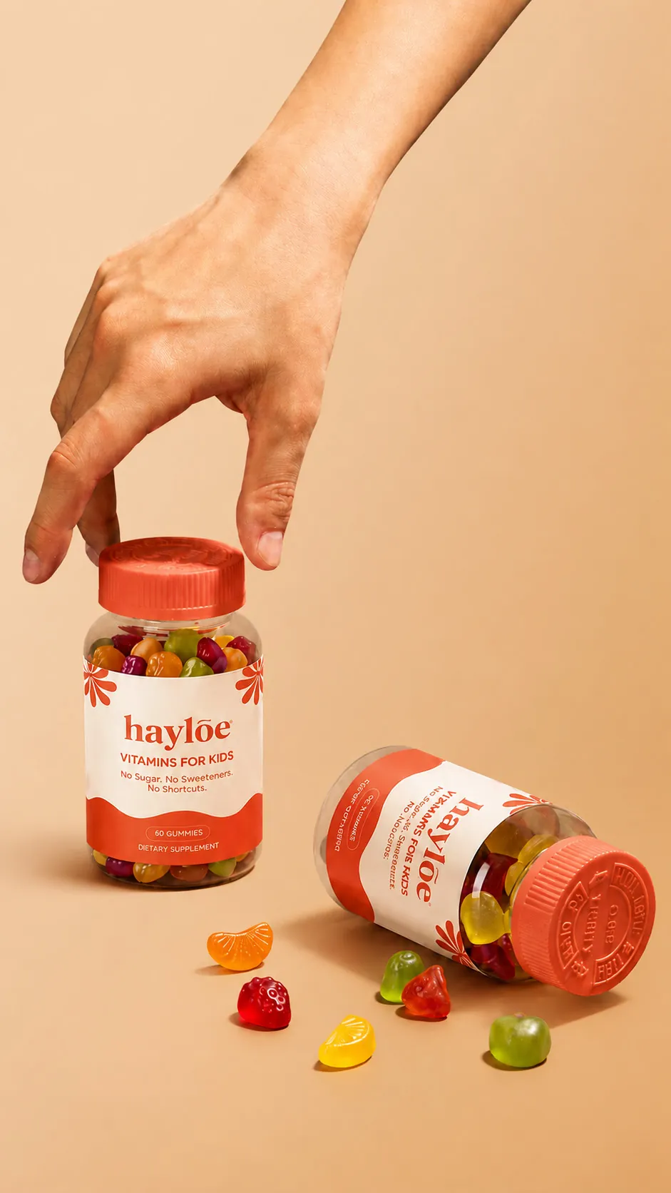 A hand lifts a jar of Hayloe gummies, with a second jar tipped over and gummies spilling out